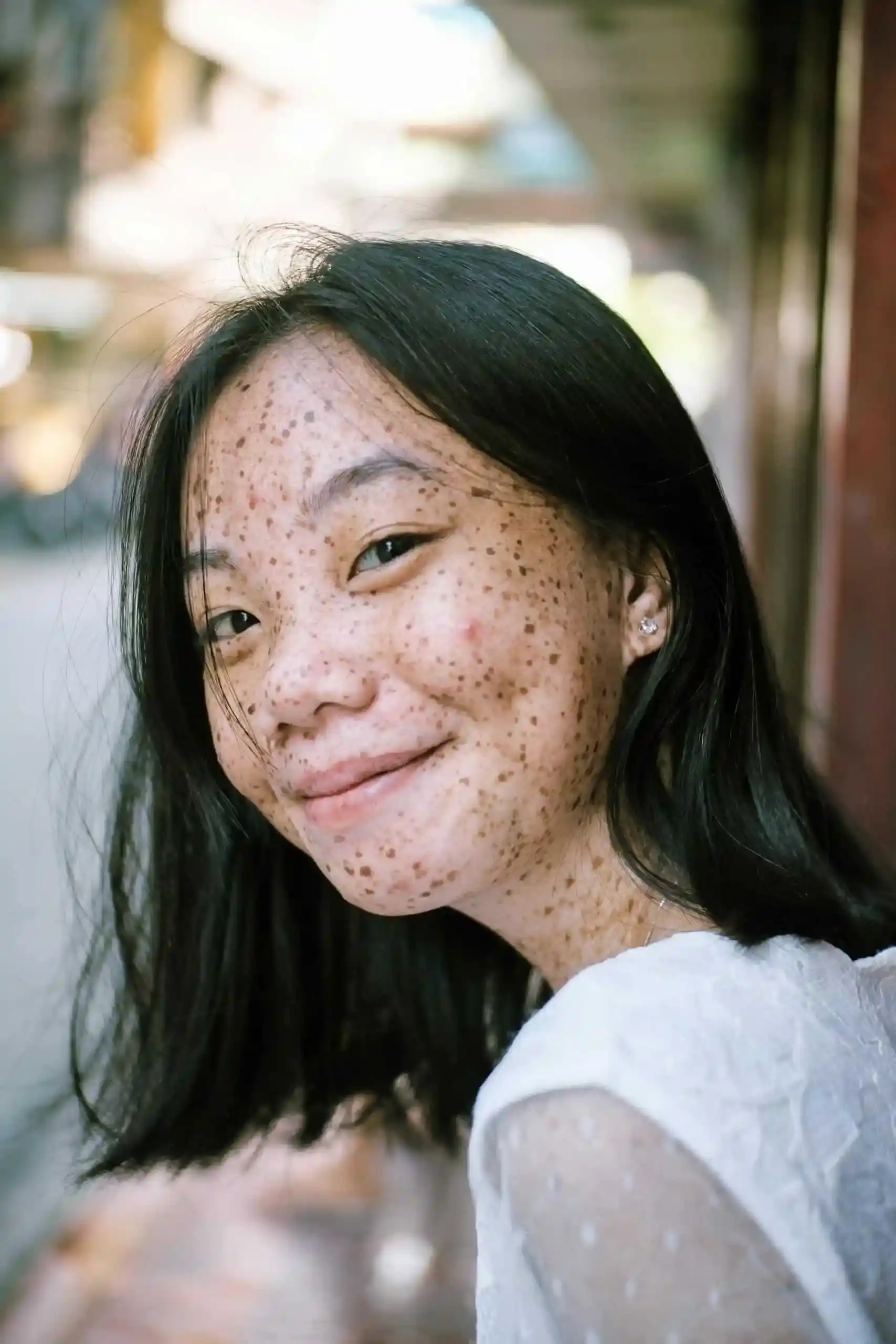 Close-up portrait of a smiling young woman with freckles, capturing a natural and joyful expression outdoors.