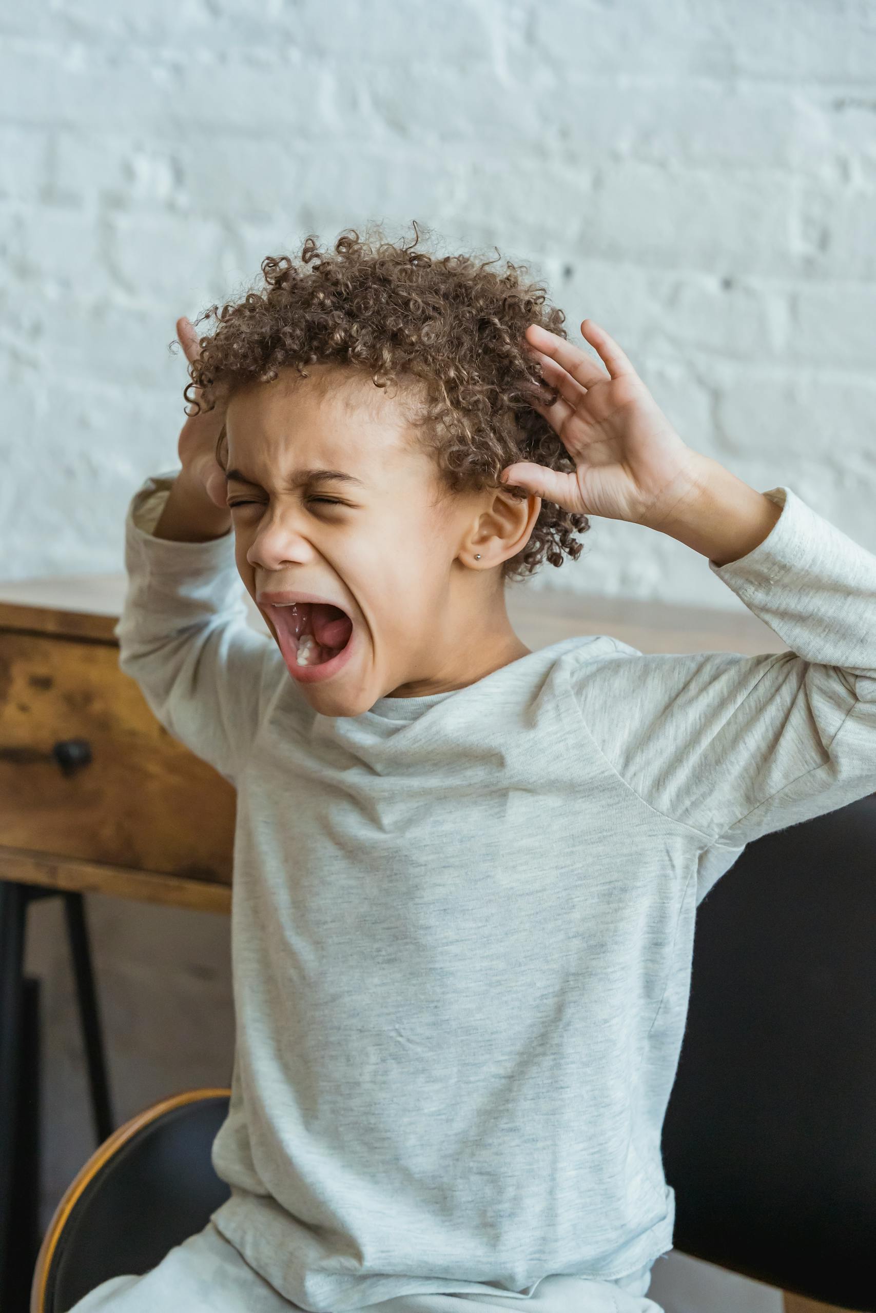Young black child showing frustration in an indoor setting, hands on head in distress