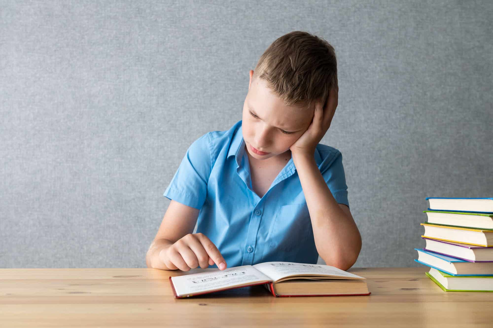 Young Boy Concentrating on Reading Books at Desk. World Dyslexia Awareness Day